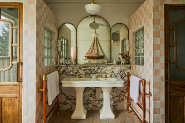 Salle de bain avec double vasque en marbre, miroirs arqués et robinetterie vintage en laiton