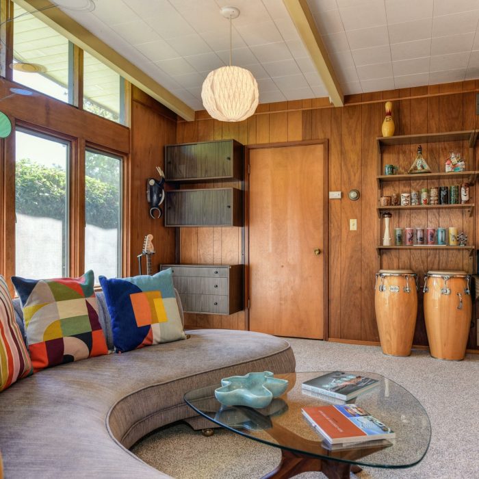 Salon mid-century chaleureux avec canapé courbe, table basse en verre et murs en bois, baigné de lumière naturelle.
